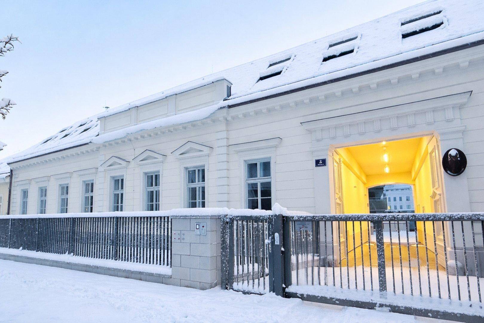 Elegante Fassade des Gebäudes im Winter mit Schnee und beleuchtetem Eingangsbereich.
