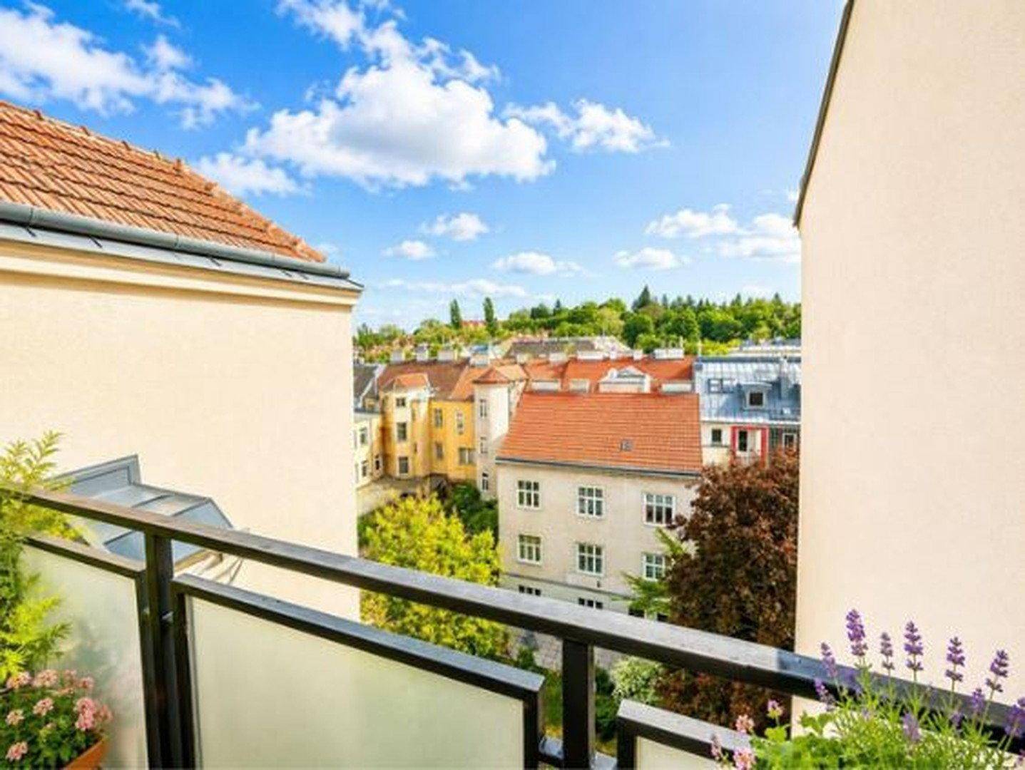Balkon mit Blick auf die umliegenden Gebäude und grüne Bäume unter blauem Himmel.