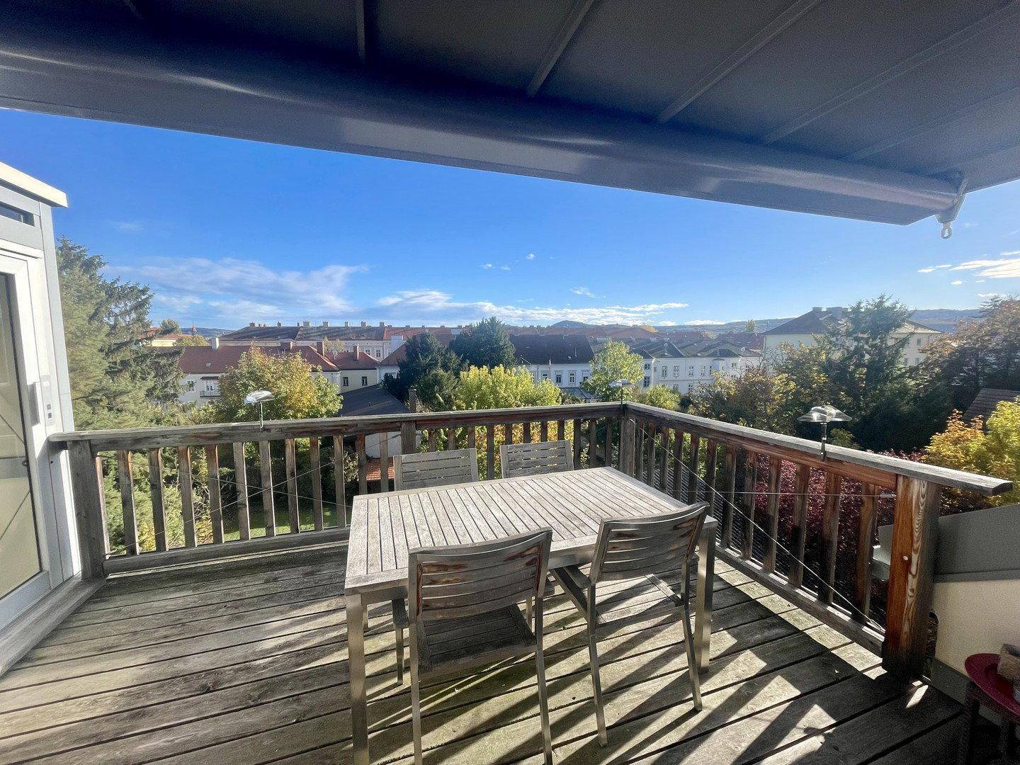 Geräumiger Holzbalkon mit Esstisch und Stühlen, bietet einen weiten Blick über die Stadt und grüne Umgebung.