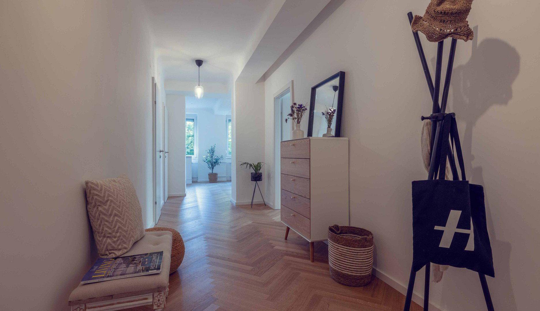 Heller Flur mit Fischgrätparkett, Garderobe und Kommode, der zu weiteren Räumen führt.