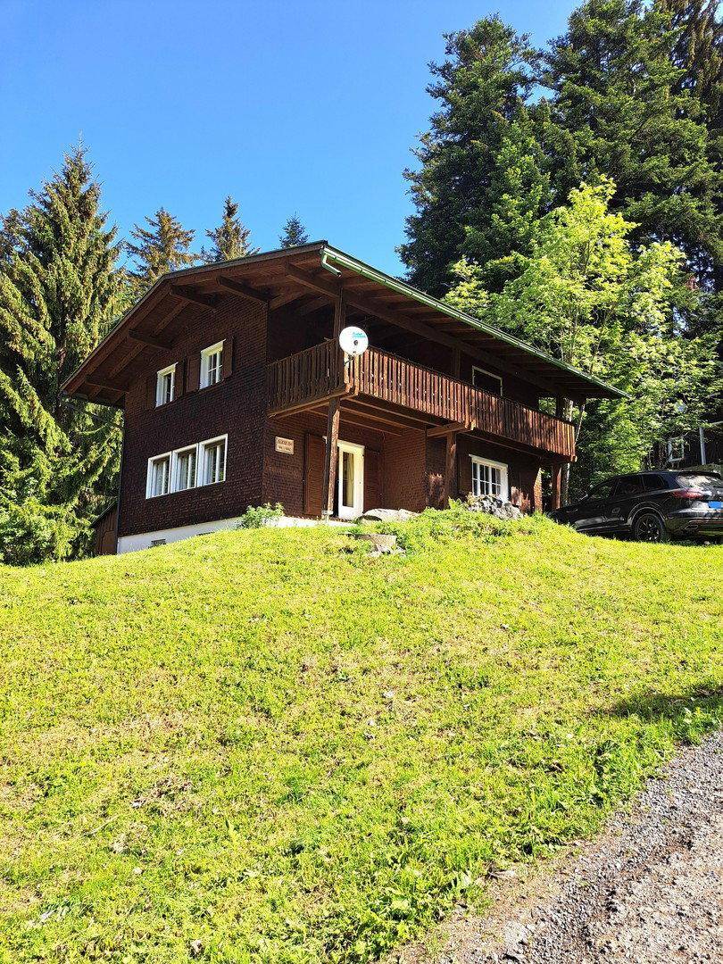 Charmantes Holzhaus in alpiner Umgebung, umgeben von üppigem Grün und hohen Bäumen.