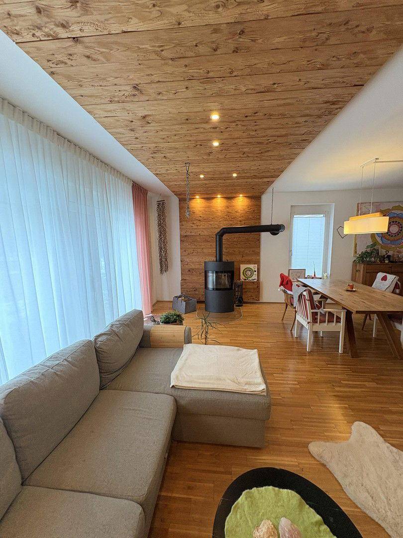Heller Wohn-Essbereich mit Holzboden, Holzdecke und einem modernen Holzofen als Blickfang.