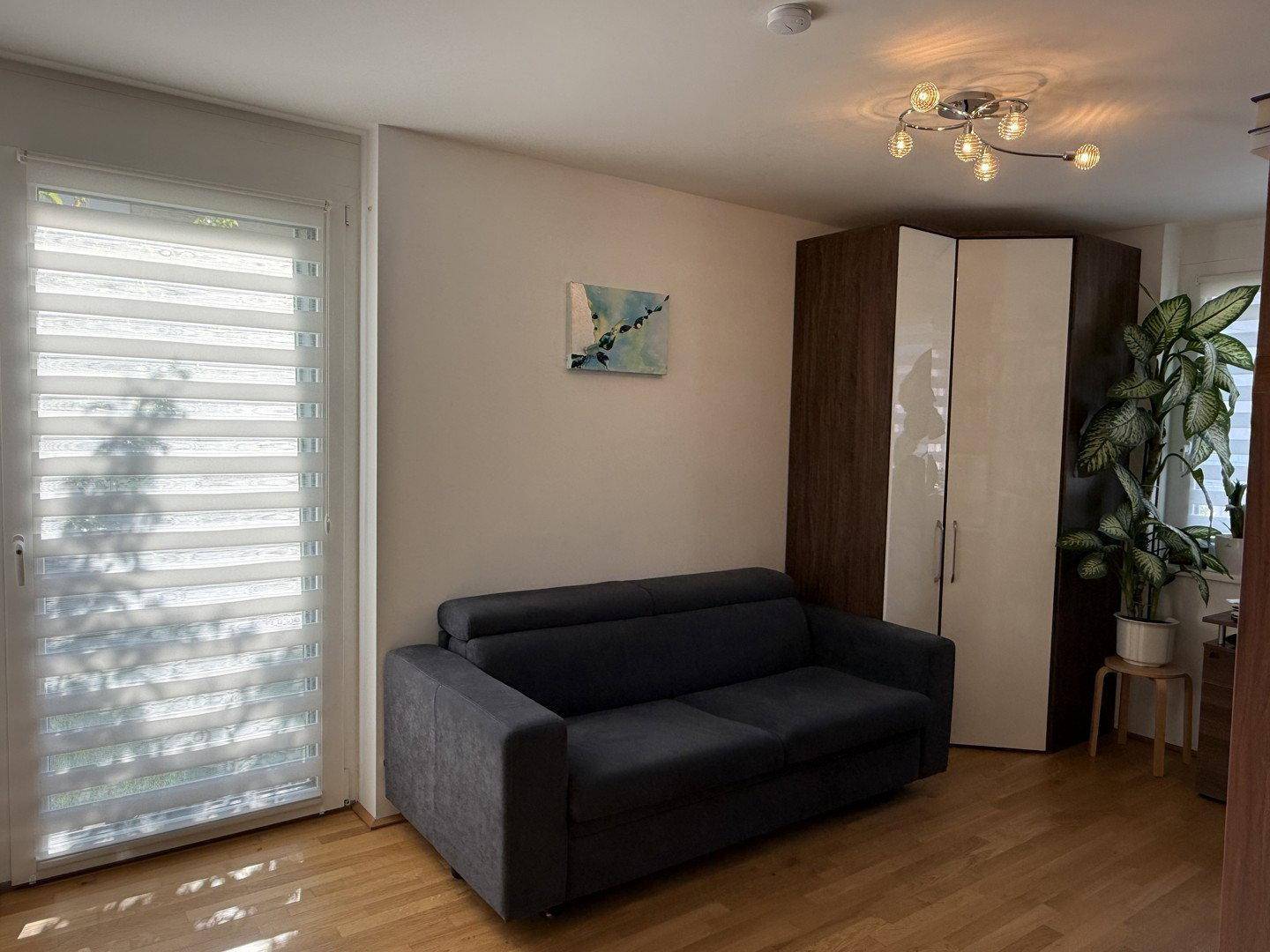 Helles Zimmer mit Schlafsofa, Holzboden und Zugang zu einem Balkon oder Garten.