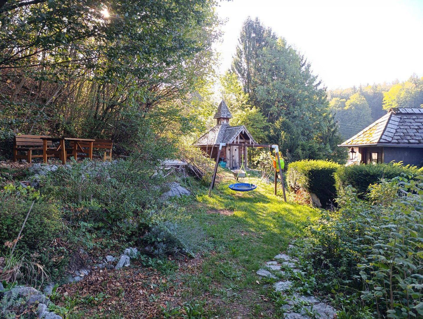 Naturbelassener Gartenbereich mit kleiner Holzlaube, Schaukel und üppiger Vegetation.