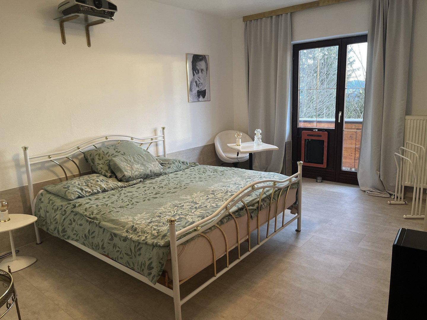 Helles Schlafzimmer mit Doppelbett, kleinem Beistelltisch und Zugang zum Balkon mit Winteraussicht.