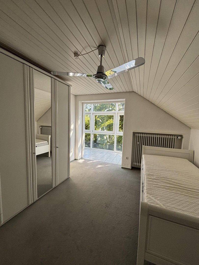 Helles Schlafzimmer im Dachgeschoss mit Dachschrägen, Deckenventilator und Zugang zum Wintergarten.