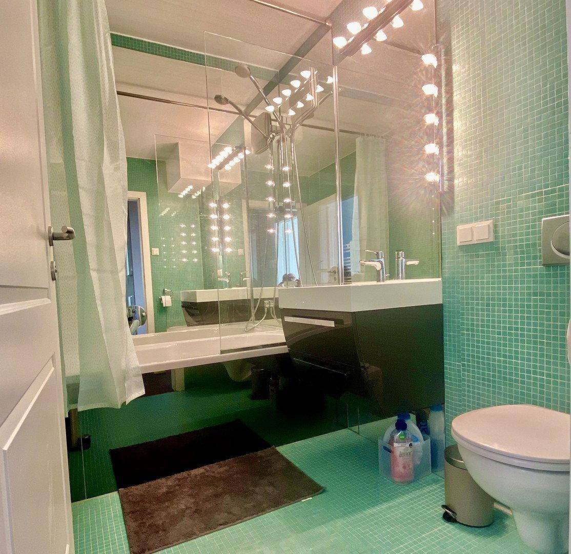 Modernes Badezimmer mit grünen Mosaikfliesen, großem Spiegel und stilvollem Waschbecken.
