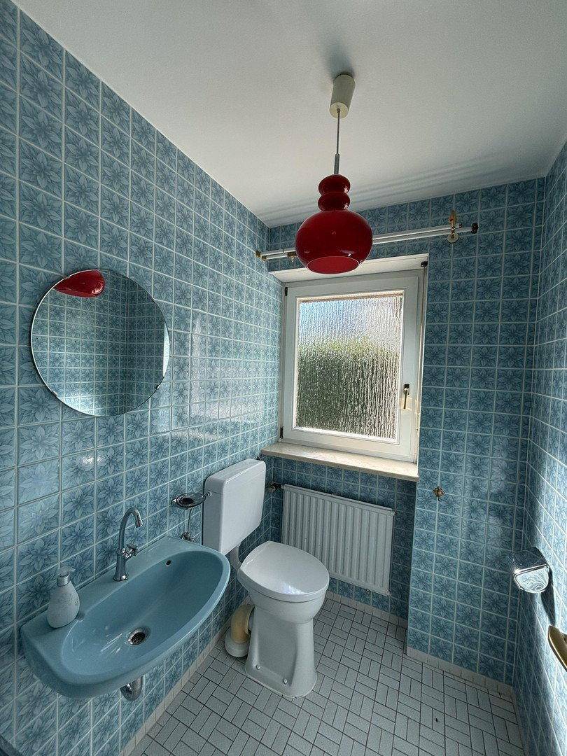 Kleines Gäste-WC mit blauen Fliesen, Fenster und roter Deckenleuchte.