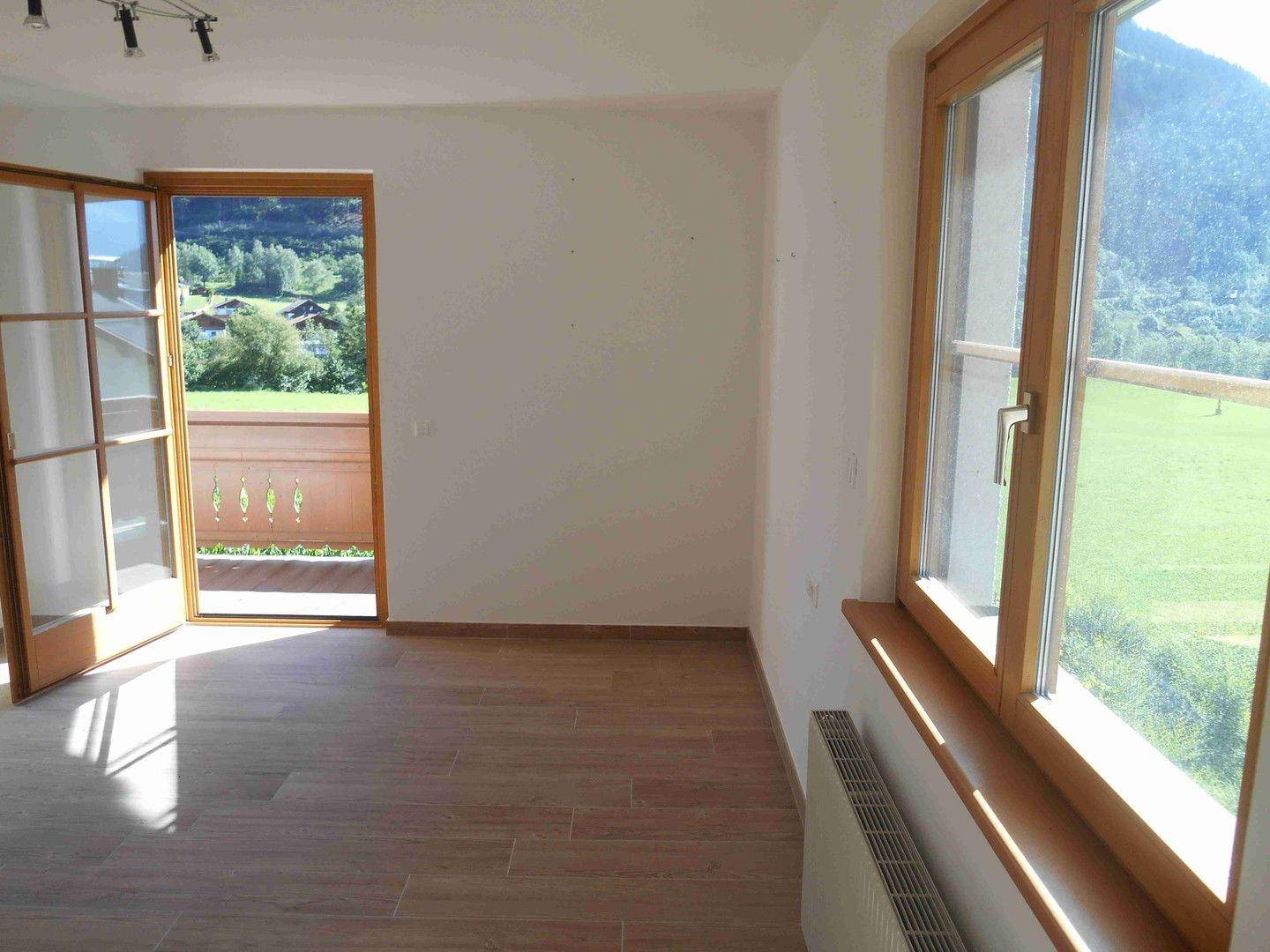 Helles Wohnzimmer mit Fliesenboden, Balkonzugang und weitem Blick auf die grüne Landschaft.