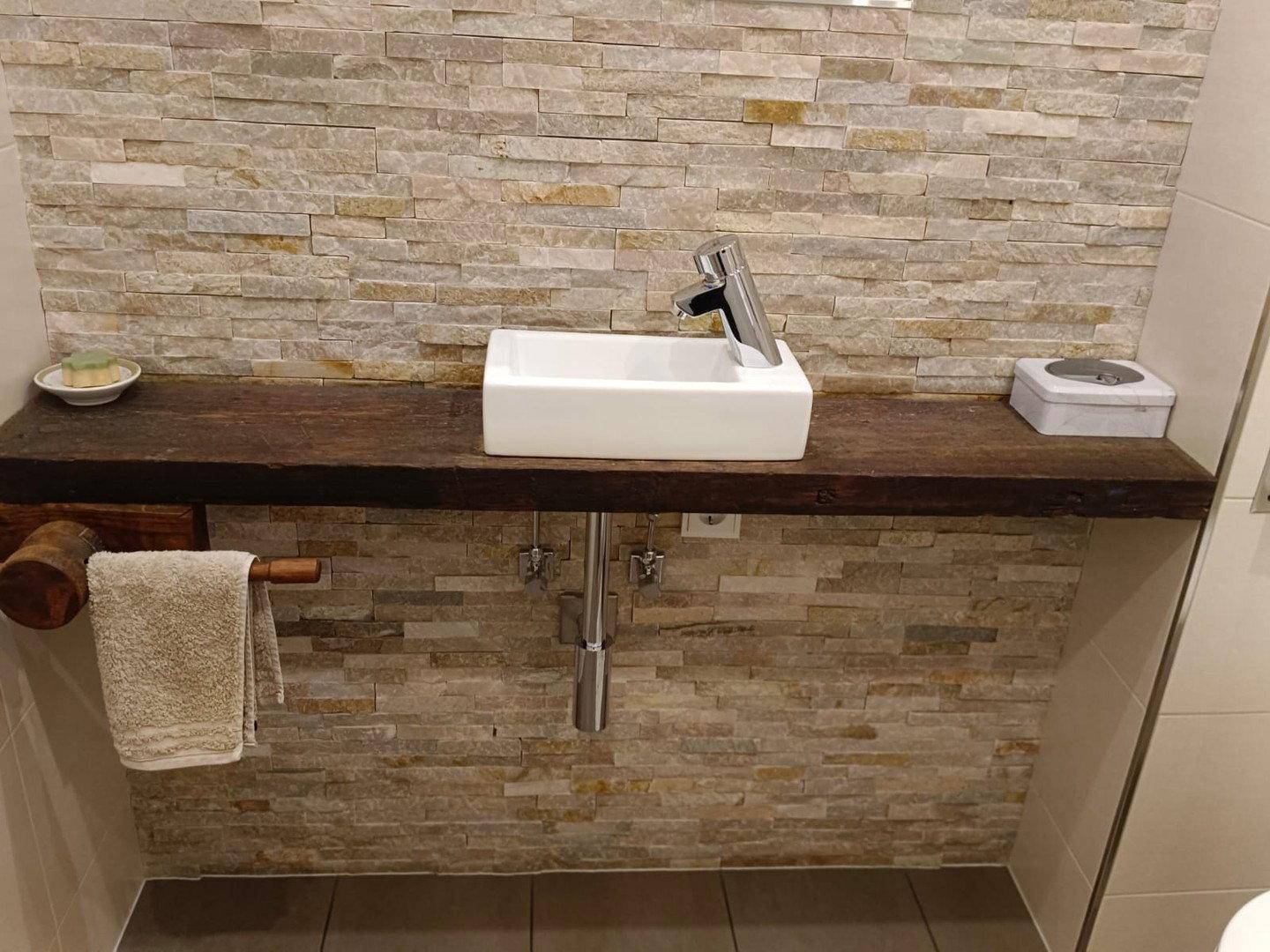 Modernes Badezimmer mit Aufsatzwaschbecken auf Holzplatte und Steinwand-Akzent.
