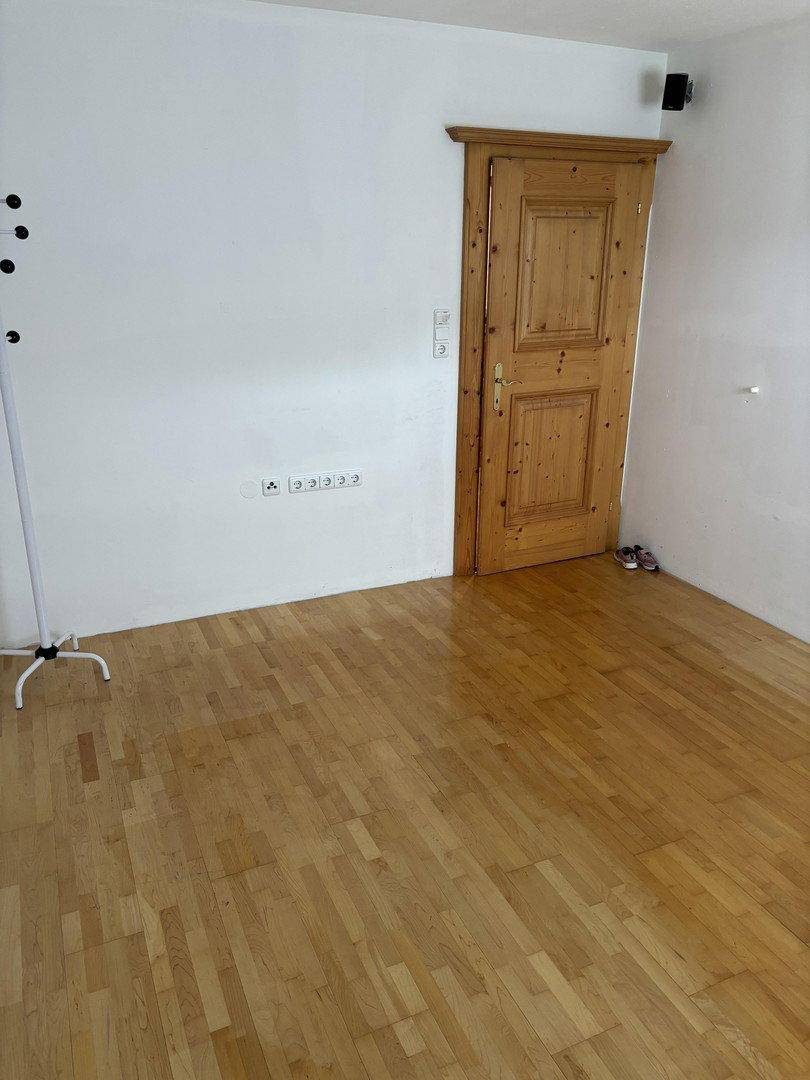 Leerer Raum mit hellem Parkettboden, weißen Wänden und einer traditionellen Holztür.