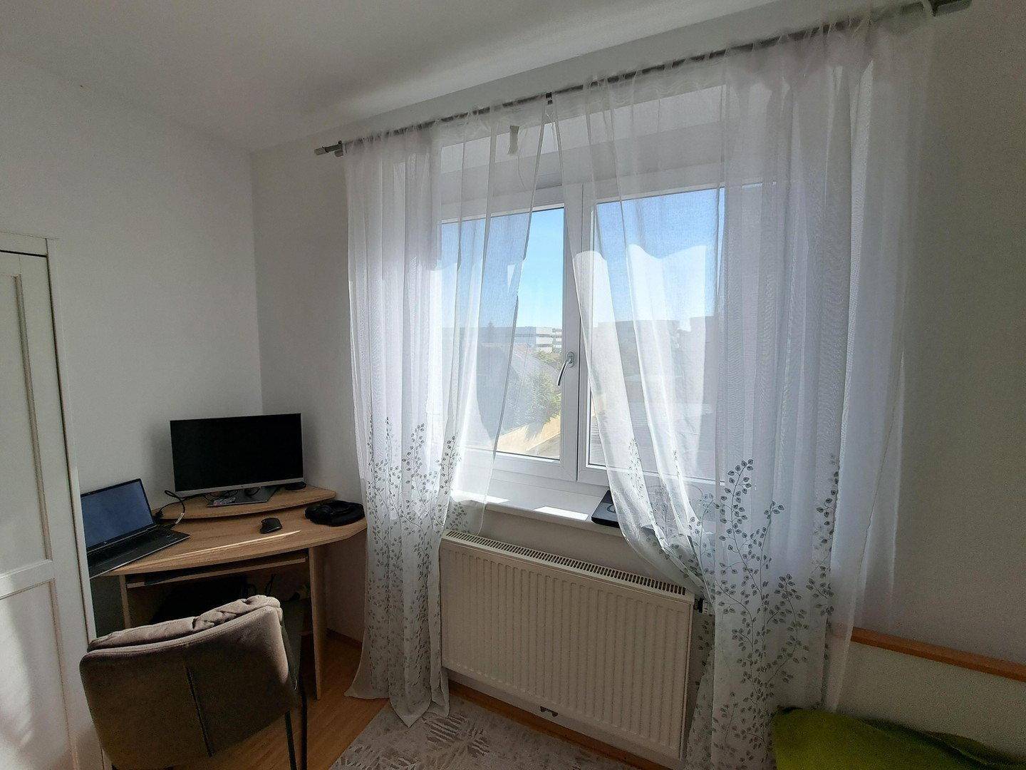 Helles Schlafzimmer mit Schreibtisch, Laptop und Blick ins Grüne.