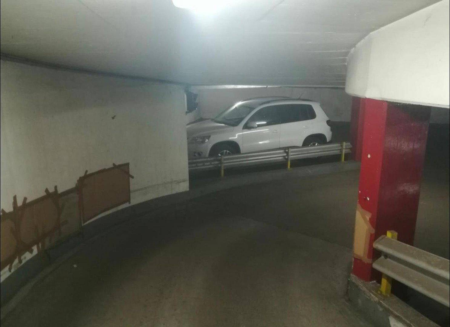 Innenansicht einer Tiefgarage mit einer Kurve und einem geparkten weißen Auto an der Seite.