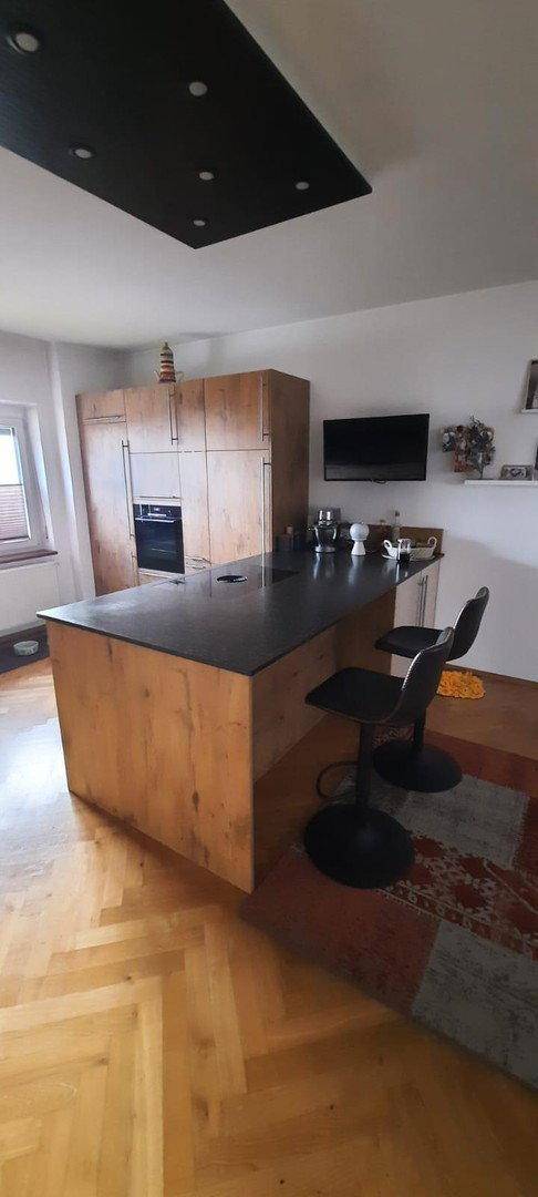 Stilvolle Kücheninsel mit dunkler Arbeitsplatte und integrierten Geräten, ergänzt durch warmen Parkettboden.