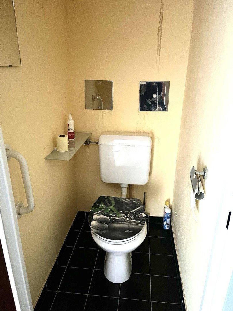 Kleines WC mit Toilette, Ablagefläche, Haltegriffen und gelben Wänden.
