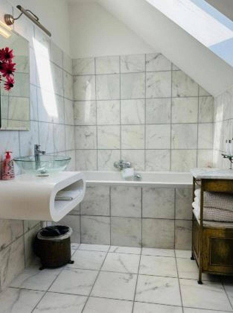 Modernes Badezimmer mit Marmorfliesen, Badewanne, Glaswaschbecken und Dachfenster für Tageslicht.