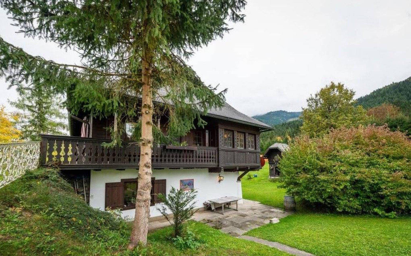 Charmantes Landhaus mit Holzbalkonen und üppiger Vegetation in bergiger Umgebung.