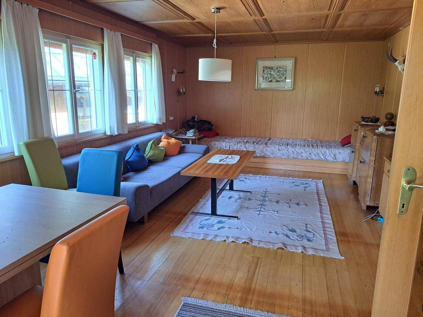 Gemütlicher Wohn- und Essbereich mit Holzvertäfelung, Holzboden und farbigen Stühlen.