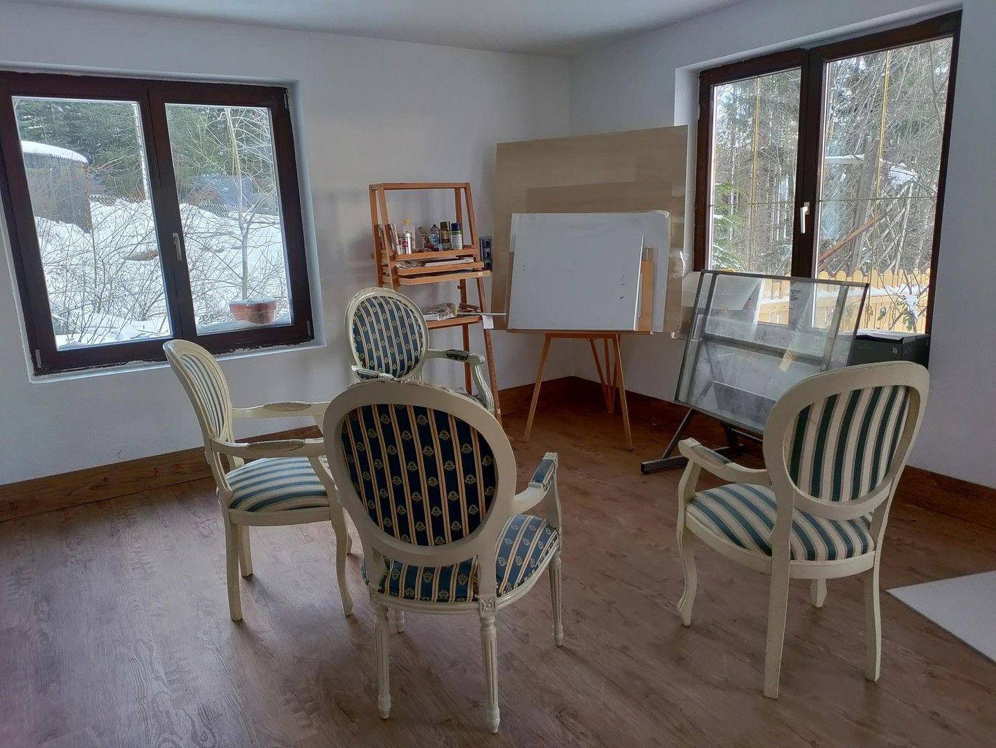 Heller Raum mit Holzboden, Fenstern und Stühlen, bereit für die Einrichtung.