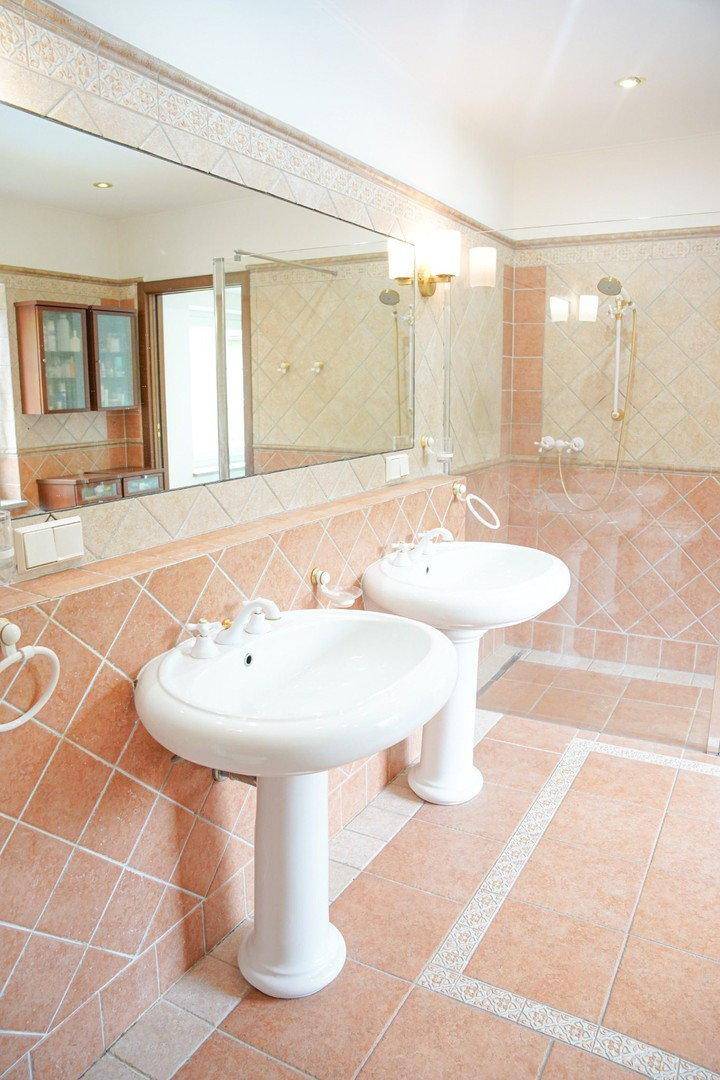 Zwei klassische Waschbecken mit großem Spiegel in einem gefliesten Badezimmer.