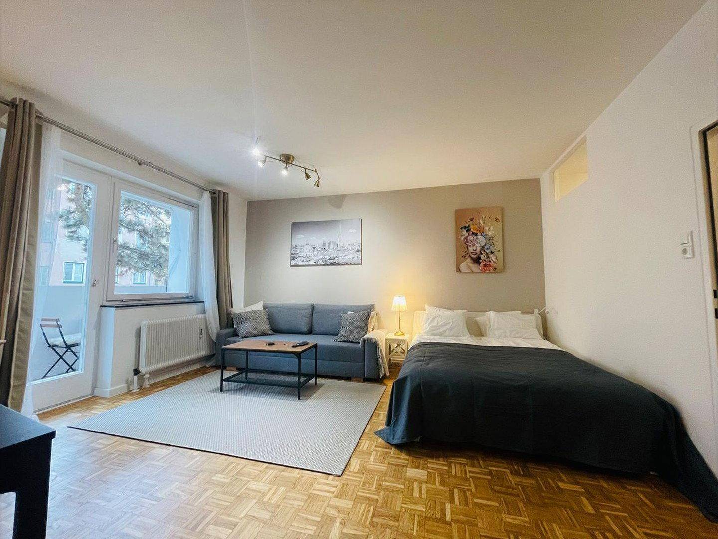 Heller Wohn- und Schlafbereich mit Balkonzugang, Sofa, Bett und Holzboden.