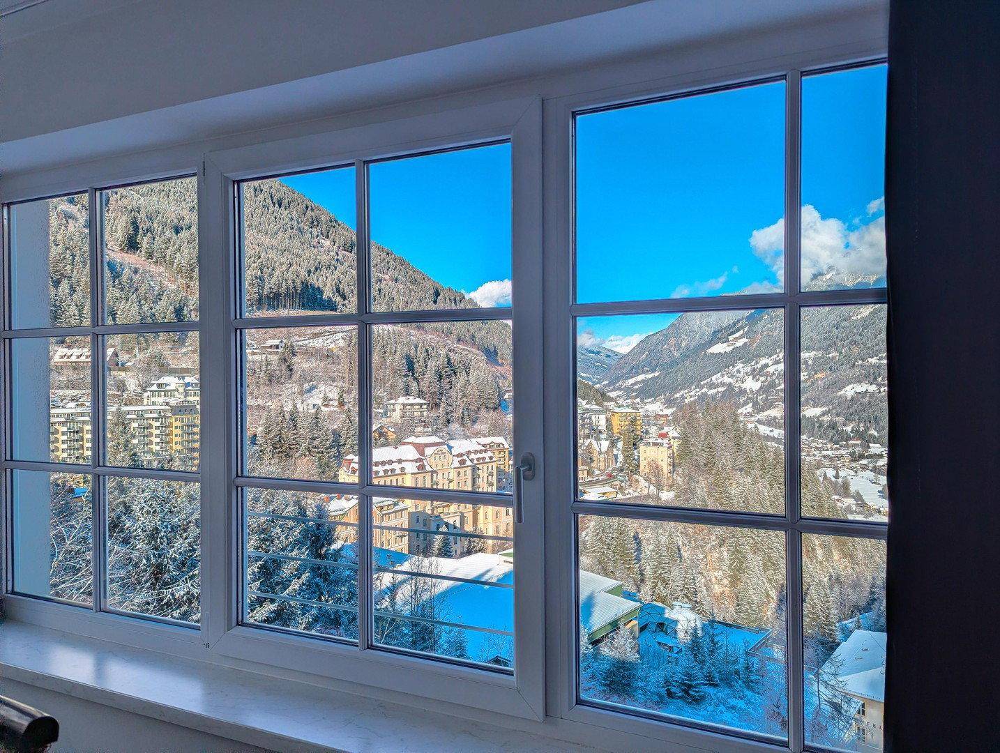 Fenster mit weitem Blick auf die verschneite Berglandschaft und das winterliche Dorf.
