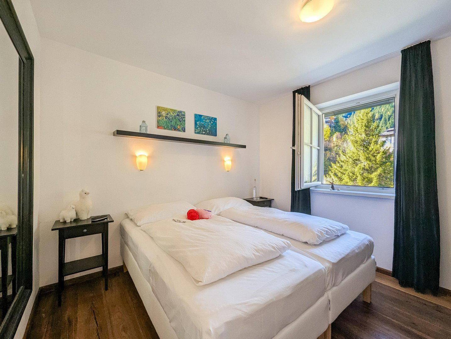 Helles Schlafzimmer mit Doppelbett, großem Spiegel und Fenster mit Blick auf die Natur.