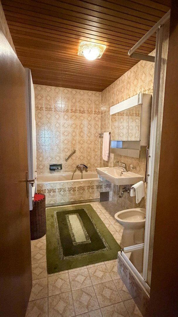 Badezimmer im 80er-Jahre-Stil mit Badewanne, Waschbecken und Duschbereich.
