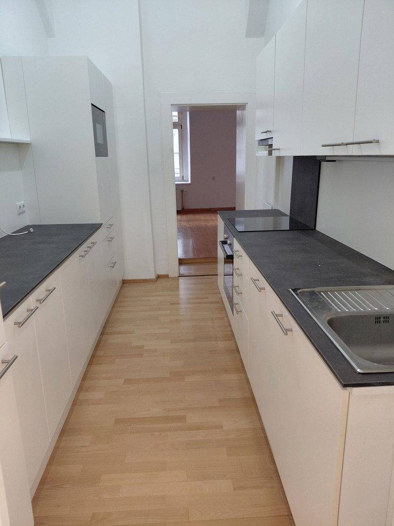 Moderne Einbauküche mit weißen Schränken, dunklen Arbeitsplatten und Holzboden.