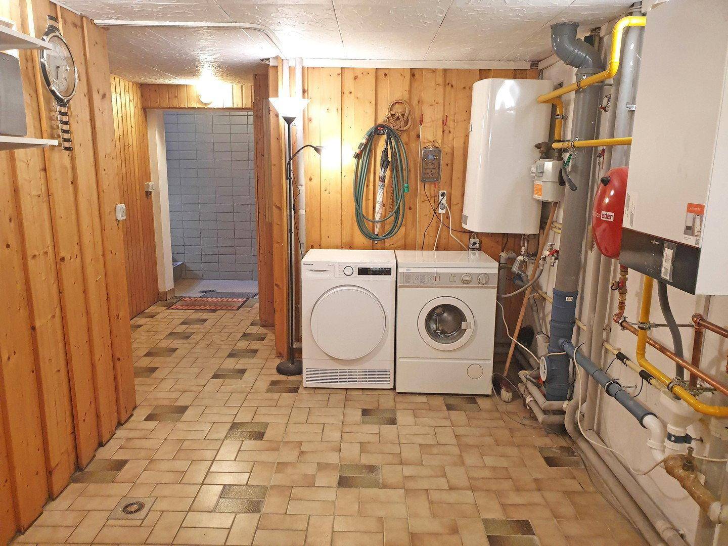 Hauswirtschaftsraum im Keller mit Waschmaschine, Trockner und sichtbaren Heizungsanlagen.