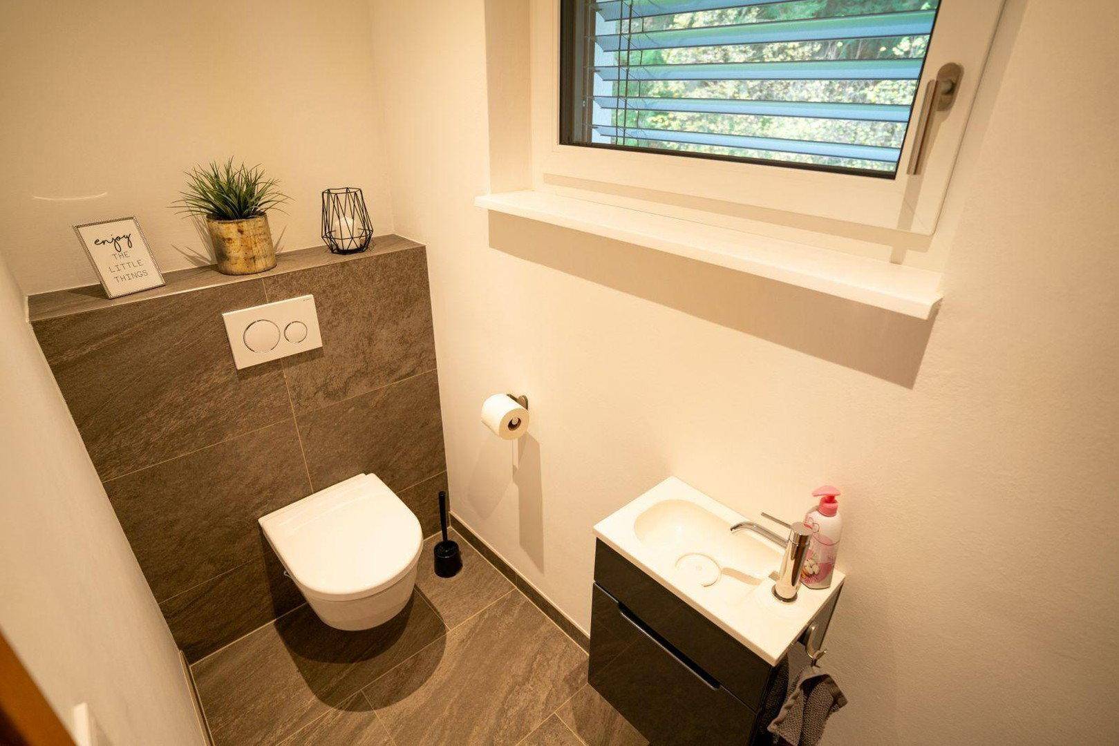 Kleines Gäste-WC mit wandhängender Toilette, Waschbecken und Fenster.