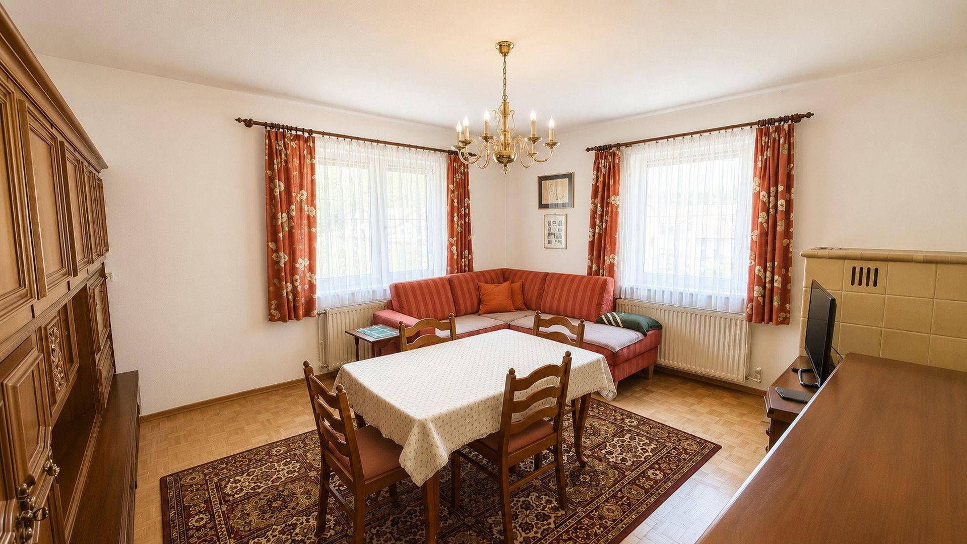 Gemütlicher Wohn- und Essbereich mit traditionellen Möbeln, Teppich und Kachelofen.