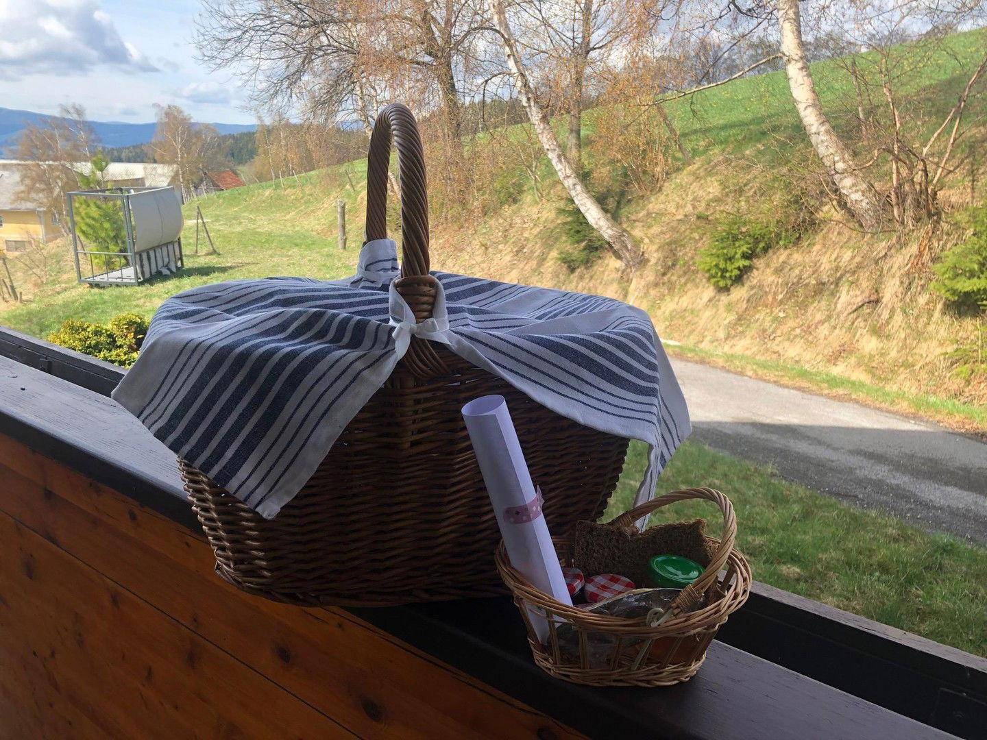 Picknickkorb auf einem Holzbalkon mit Blick auf die grüne Hügellandschaft.