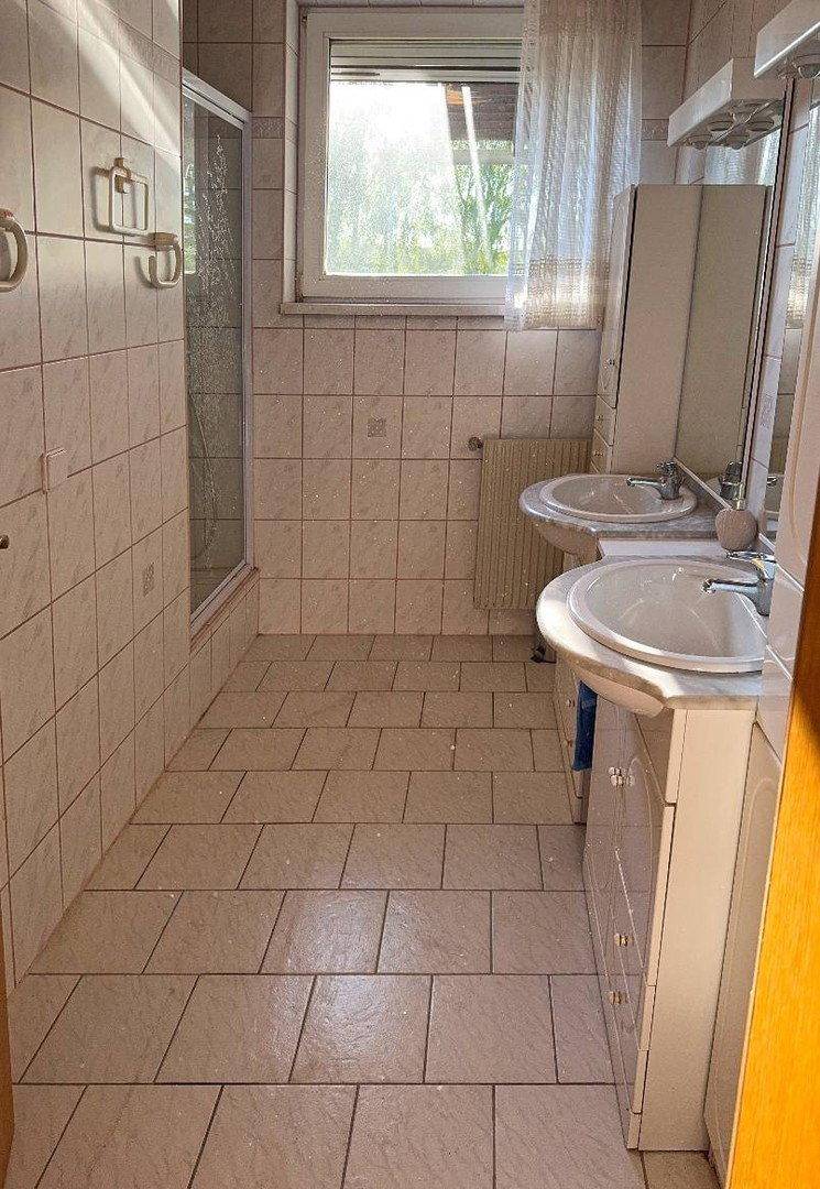 Badezimmer mit zwei Waschbecken, Duschkabine und Fenster für natürliches Licht.