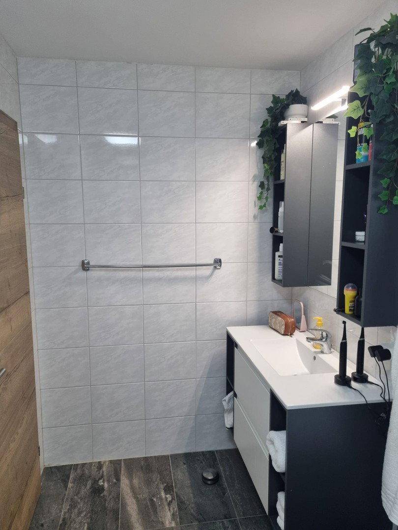 Badezimmer mit modernem Waschtisch, Spiegel und dunklem Boden in einem gepflegten Zustand.