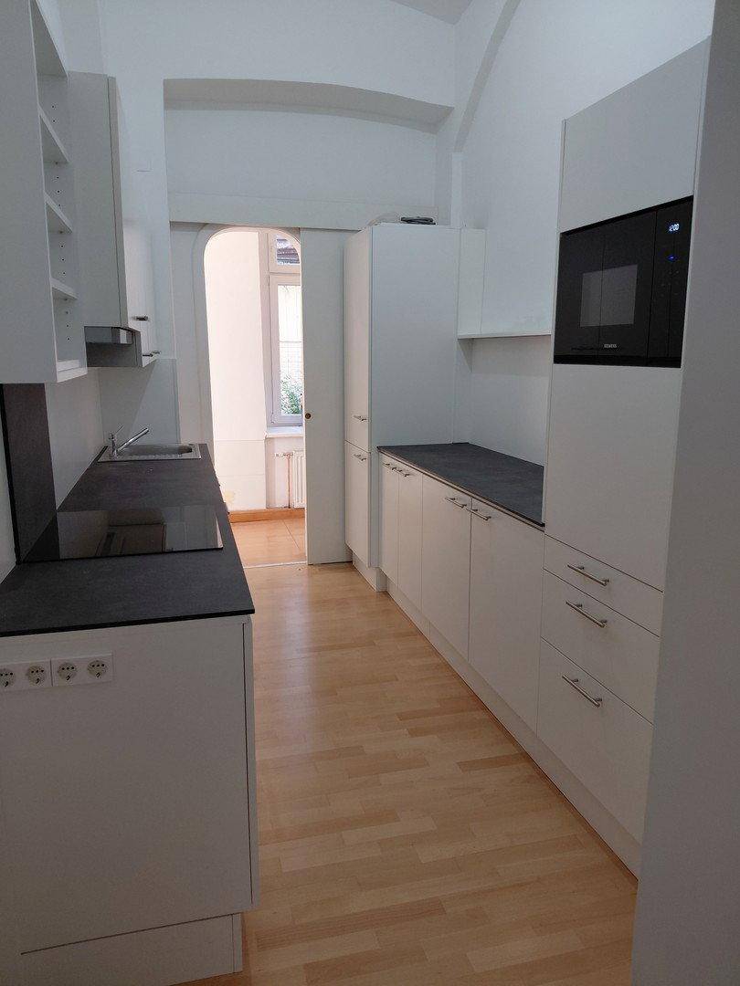 Lange, schmale Küche mit weißen Schränken, integriertem Backofen und Holzboden.