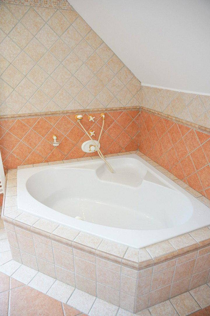 Nahaufnahme einer gefliesten Eckbadewanne mit Armaturen in einem Badezimmer.