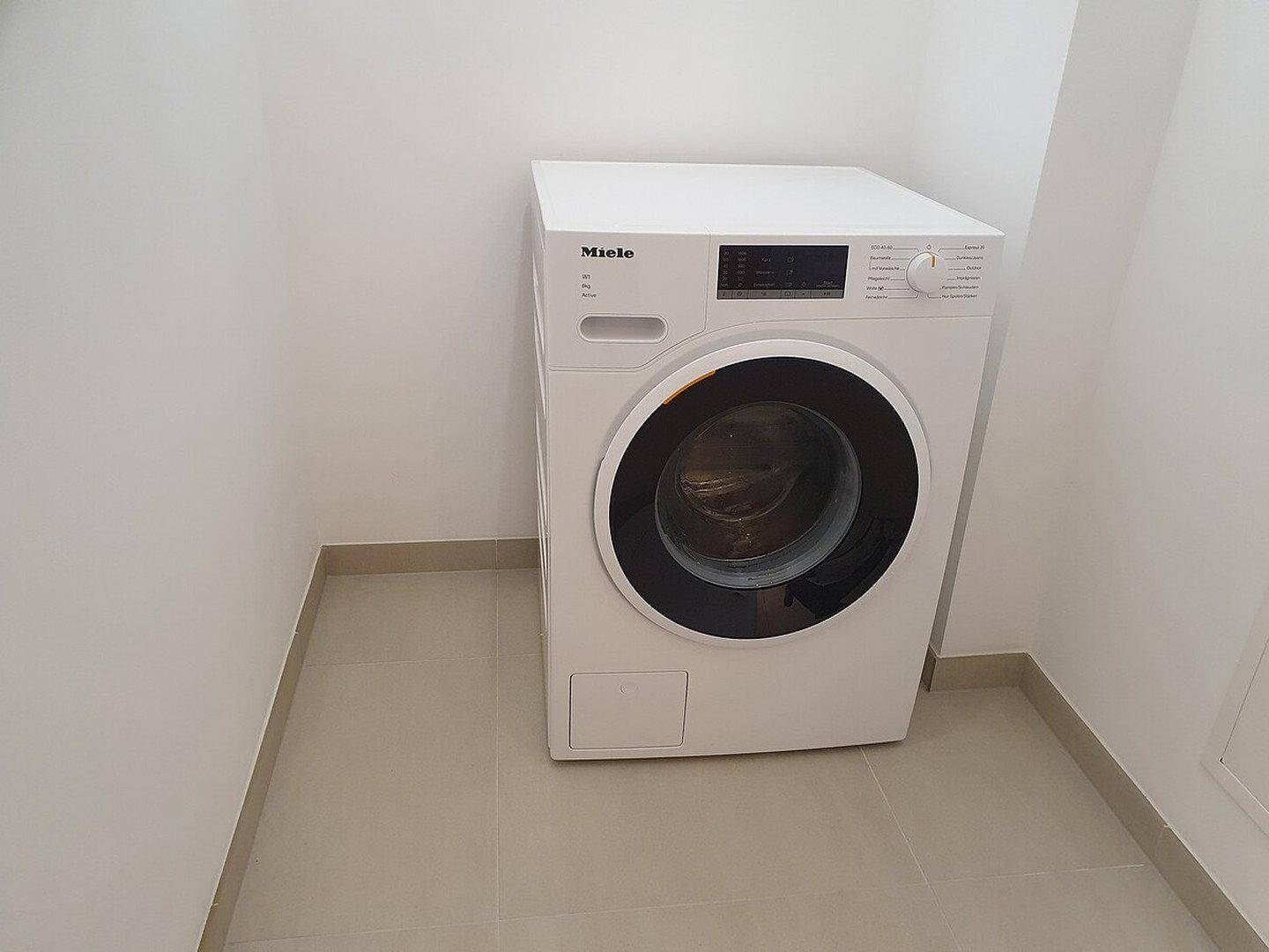 Praktischer Hauswirtschaftsraum mit einer Miele Waschmaschine auf Fliesenboden.