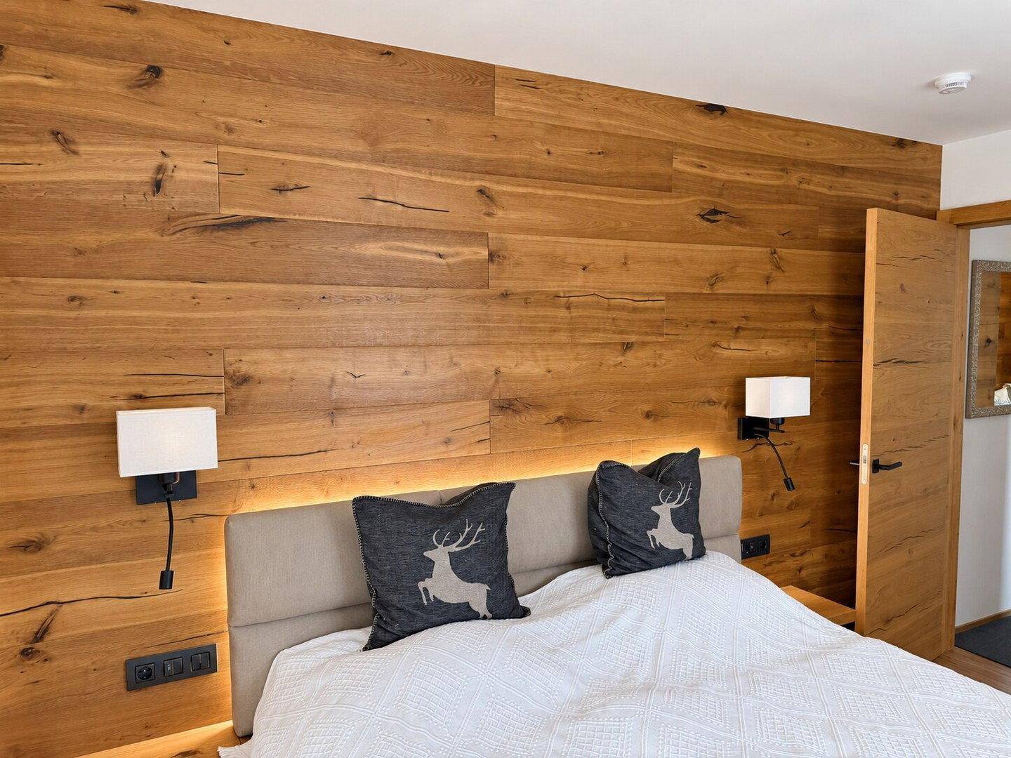 Schlafzimmer mit Holzwandverkleidung, gepolstertem Kopfteil und indirekter Beleuchtung für Gemütlichkeit.
