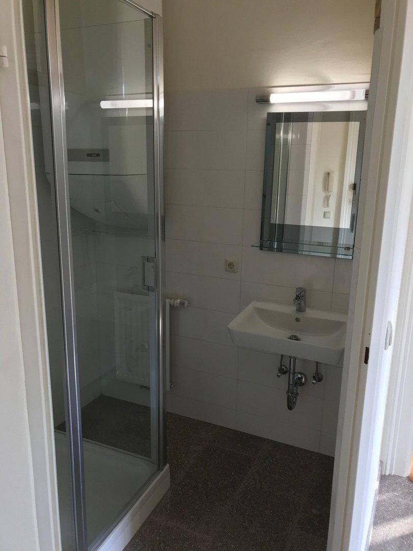 Funktionales Badezimmer mit Duschkabine, Einzelwaschbecken und Spiegelschrank, komplett gefliest.