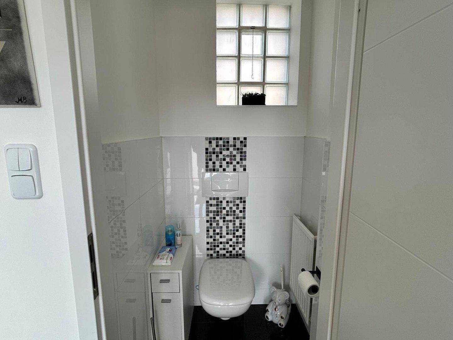 Modernes Gäste-WC mit weißen Fliesen, Glasbausteinfenster und wandhängendem WC.