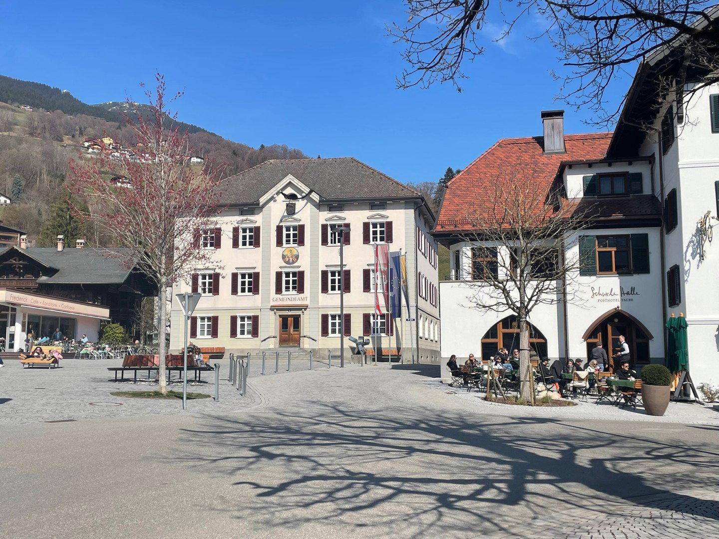 Belebtes Stadtzentrum mit traditionellen Gebäuden und Außengastronomie unter blauem Himmel.