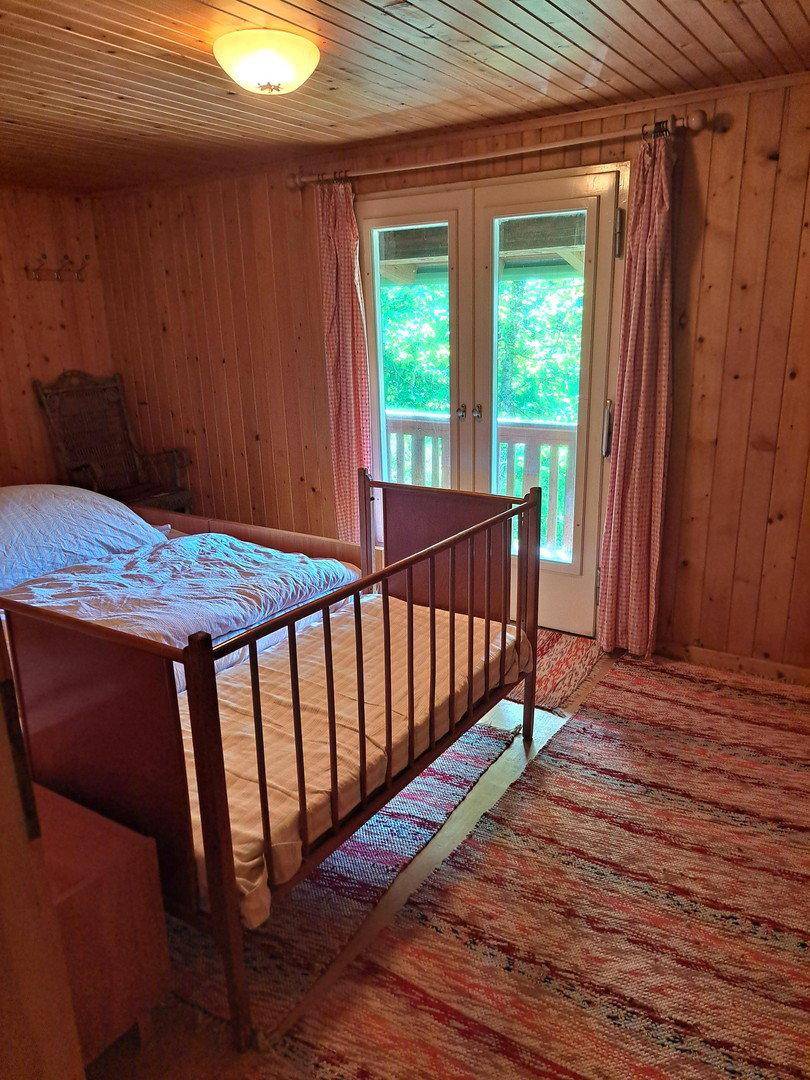Gemütliches Schlafzimmer mit Holzboden und Zugang zu einem Balkon, umgeben von Holzvertäfelung.