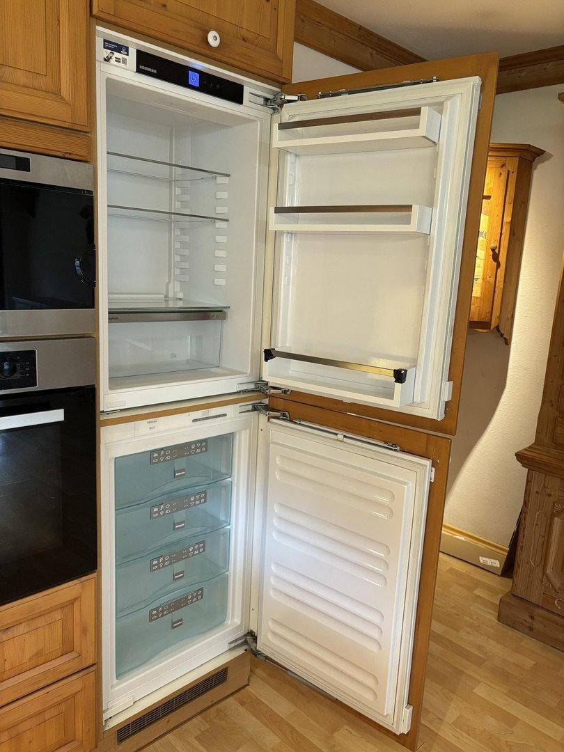 Offener Einbaukühlschrank und Gefrierschrank in einer traditionellen Holzküche mit modernen Geräten.