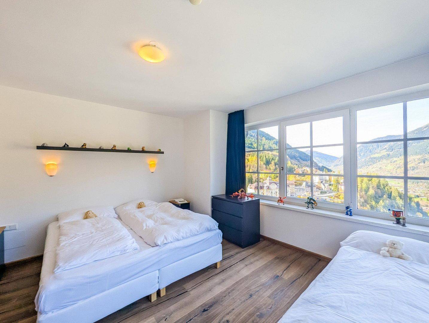 Schlafzimmer mit zwei Betten und weitem Blick auf die Berge und das Tal durch große Fenster.
