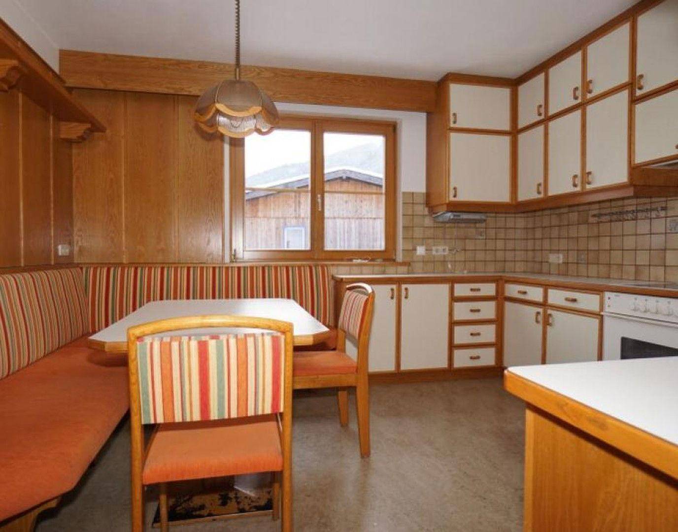 Traditionelle Wohnküche mit Holzelementen, Einbauküche und gemütlicher Sitzecke am Fenster.