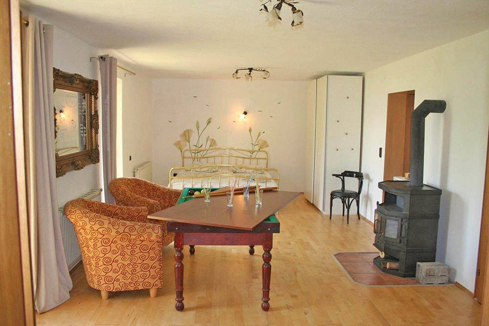 Gemütlicher Wohnbereich mit Holzboden, Kaminofen und floraler Wanddekoration.