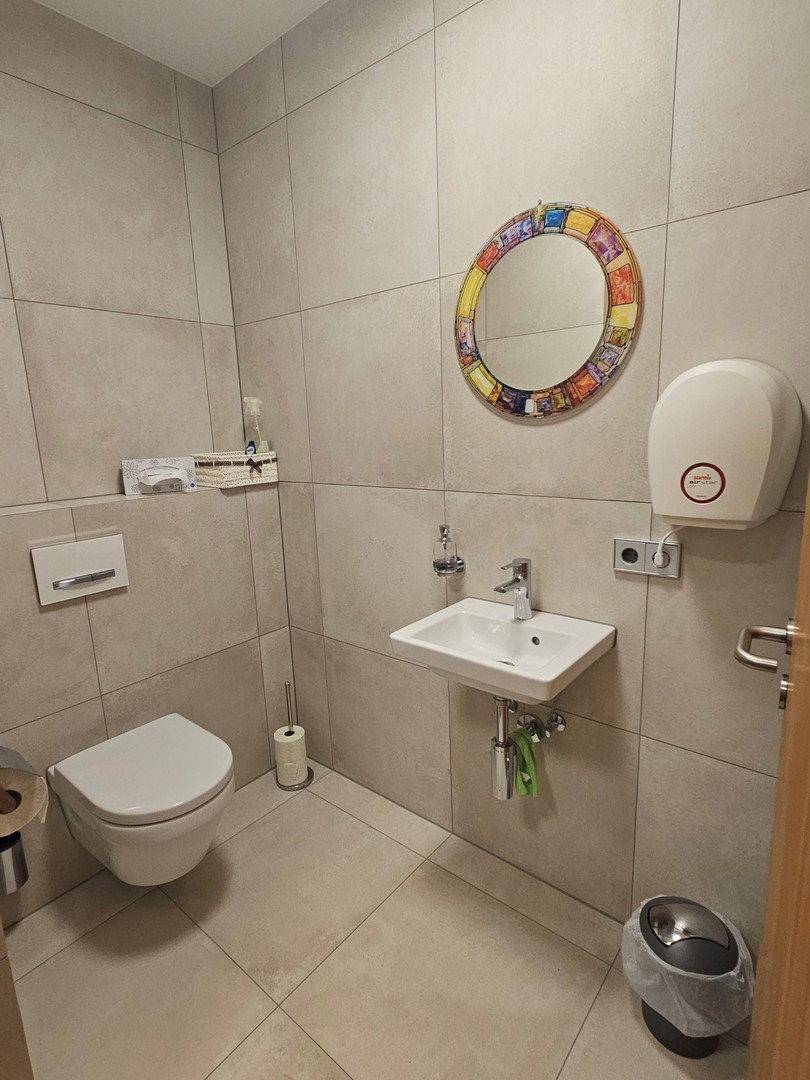 Modernes Gäste-WC mit Wand-WC, kleinem Waschbecken und farbenfrohem Spiegel.