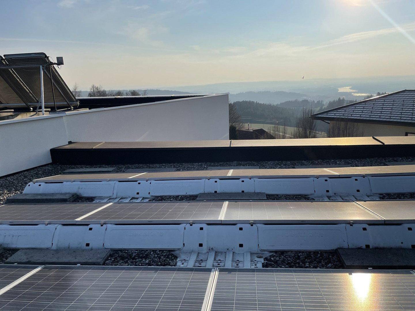 Dachfläche mit Photovoltaikanlage und weitem Blick über die hügelige Landschaft.