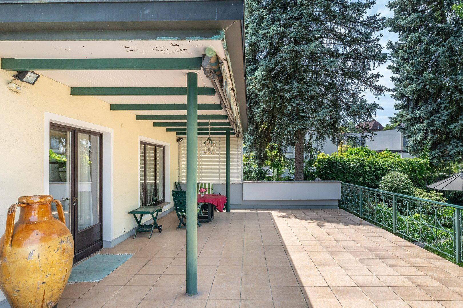 Überdachte Terrasse mit Fliesenboden und Blick auf den grünen Gartenbereich.